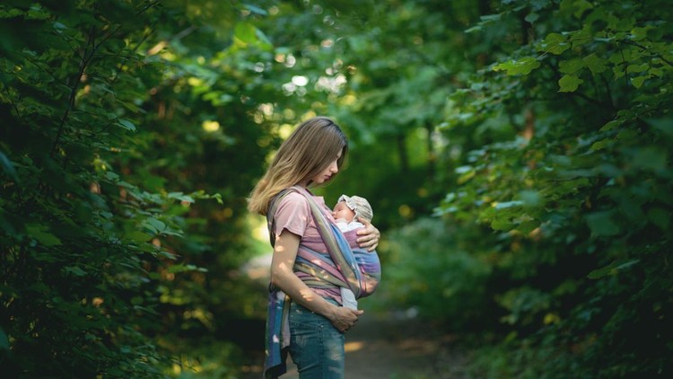 Young Mom carrying her daughter in a sling during their outdoor walk.
