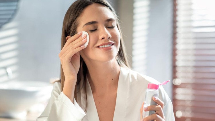 Beautiful Smiling Woman Cleansing Skin With Micellar Water And Cotton Pad While Making Daily Beauty Routine In Bathroom, Attractive Young Female Enjoying Home Skincare Treatments, Copy Space