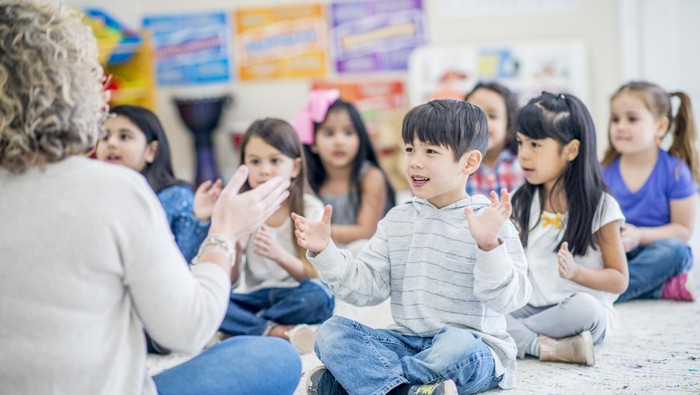 Group of kids sitting on the carpet in their kindergarten classroom.They are clapping along to music.