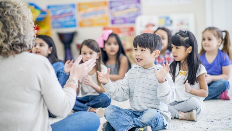 Group of kids sitting on the carpet in their kindergarten classroom.They are clapping along to music.