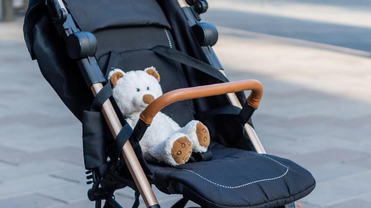Soft toy teddy bear sitting in a baby stroller on blurred background of city street