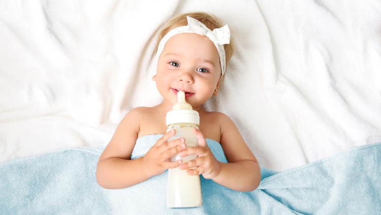 Ilustrasi Cara Memilih Susu Anak yang Bagus Baby girl with milk bottle empty space background top view.Child nutrition concept.