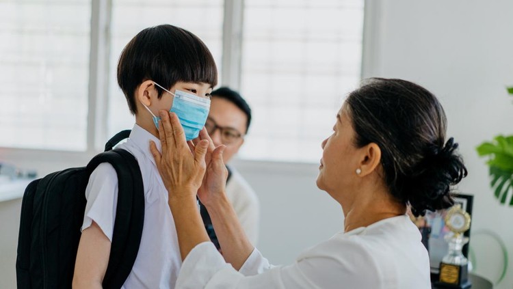 Image of an Asian grandmother helping her grandson wear a protective face mask before going to school during Covid-19 pandemic