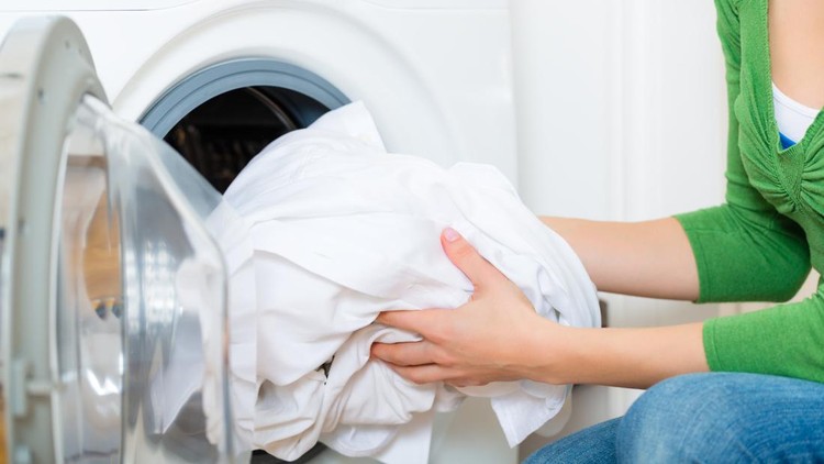 Young woman or housekeeper has a laundry day at home, she takes the laundry or whites out of your washing machine or the dryer
