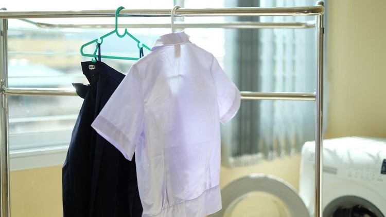 Student uniforms after washing hang on the clothes line. White shirts and blue skirts drying on clothes rack inside the house. Back to school concept.