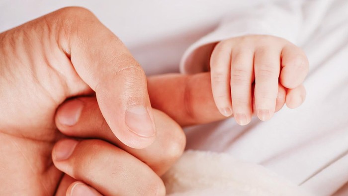 Paternity. Newborn and parent. Tiny newborn hand holding father's finger, soft color tone. Parenting, childcare and healthcare concept. Family and home concept. Health care, pediatrics.