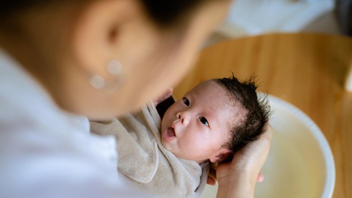 Asian mother cleaning eye her adorable baby after bathing at home.
