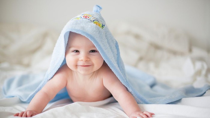 Cute little baby boy, relaxing in bed after bath, smiling happily, daytime