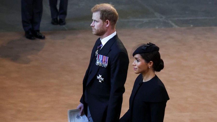 Pangeran Harry dan Meghan Markle gandengan tangan LONDON, ENGLAND - SEPTEMBER 14: Prince Harry and Meghan, Duchess of Sussex walk as procession with the coffin of Britain's Queen Elizabeth arrives at Westminster Hall from Buckingham Palace for her lying in state on September 14, 2022 in London, United Kingdom. Queen Elizabeth II's coffin is taken in procession on a Gun Carriage of The King's Troop Royal Horse Artillery from Buckingham Palace to Westminster Hall where she will lay in state until the early morning of her funeral. Queen Elizabeth II died at Balmoral Castle in Scotland on September 8, 2022, and is succeeded by her eldest son, King Charles III. (Photo by Phil Noble - WPA Pool/Getty Images)