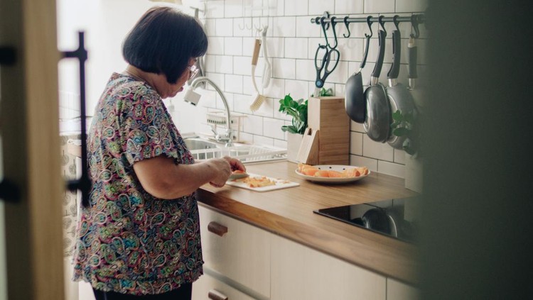 Asian grandmother hands sliced orange in kitchen at home.