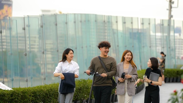 Young Asian colleagues holding takeaway food in reusable box walking in public park with e-scooter preparing their lunch break.