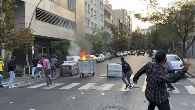 In this Tuesday, Sept. 20, 2022, photo taken by an individual not employed by the Associated Press and obtained by the AP outside Iran, protesters throw stones at anti-riot police during a protest over the death of a young woman who had been detained for violating the country's conservative dress code, in downtown Tehran, Iran. Iran faced international criticism on Tuesday over the death of a woman held by its morality police, which ignited three days of protests, including clashes with security forces in the capital and other unrest that claimed at least three lives. (AP Photo)