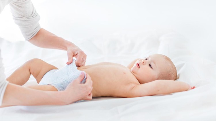 Ilustrasi Cara Memilih Popok Bayi yang Tepat Cropped shot of mother changing diaper of adorable baby boy lying on bed, 1 year old baby concept