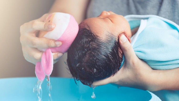Cute asian newborn baby girl take a bath. Mom cleaning her baby hair with sponge.