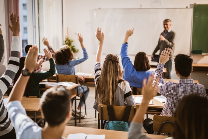 Rear view of large group of students raising their hands to answer the question on a class. Rear view of large group of students raising their hands to answer the question on a class.