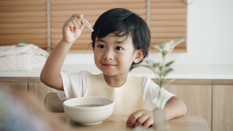 Asian baby boy and his parent eating noodle at kitchen table at home.