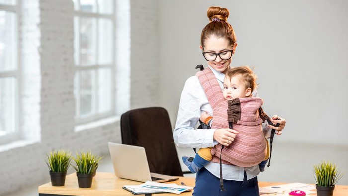 Portrait of a businesswoman standing with her baby son at the white office interior during the break