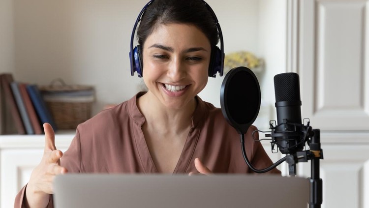 Giving voice to story. Talented indian female professional reader narrator in wireless headset record audio book using special equipment condenser microphone pop filter and sound editing app on laptop