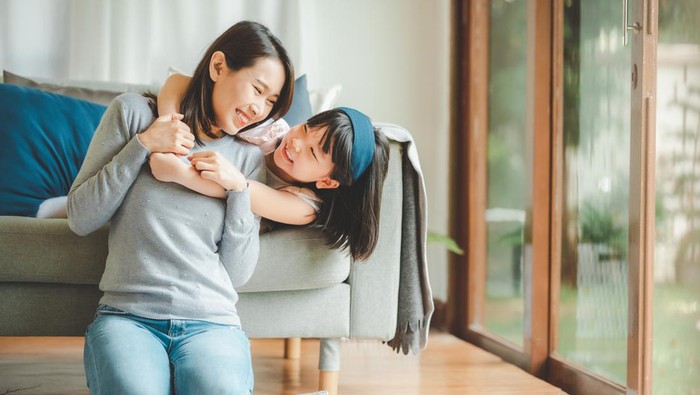 Happy Asian mother and cute little daughter having fun while playing and hugging at home in living room