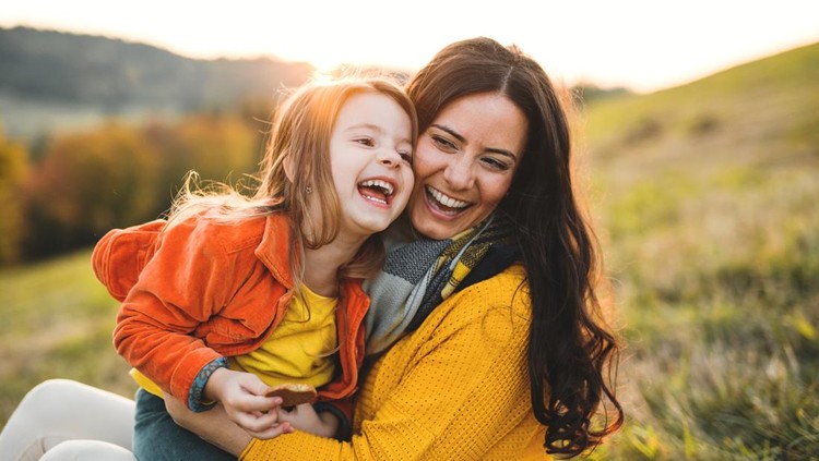 Ilustrasi Tips agar Anak Bahagia A portrait of young mother with a small daughter sitting on a ground in autumn nature at sunset.