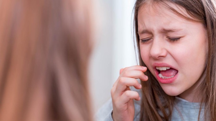 Ilustrasi Obat Sariawan untuk Anak Girl with a toothache crying in front of a mirror.