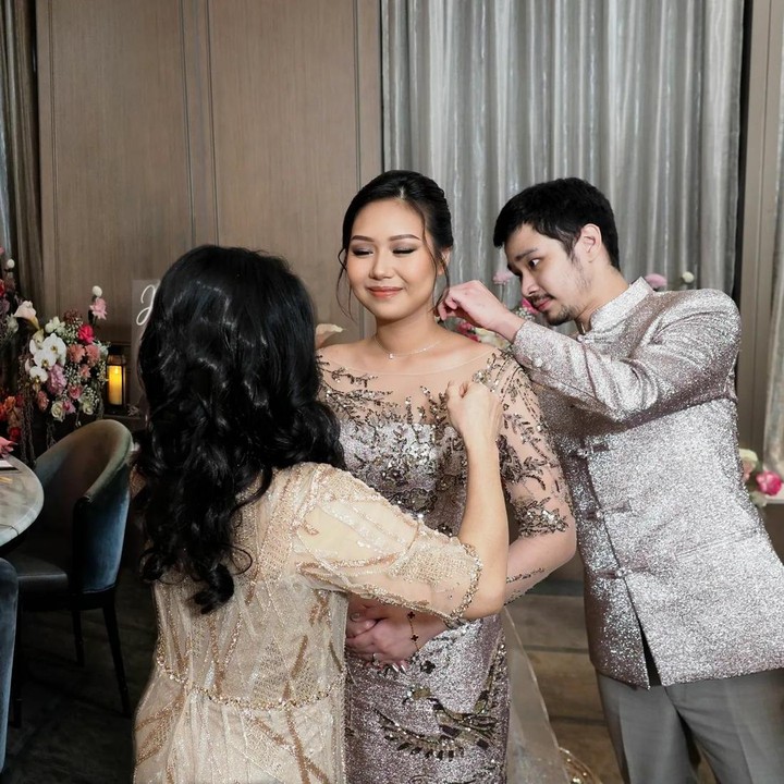 <p>Dibantu sang Bunda, Jess mengalungkan kalung kepada Sisca. Pada Tingjing, Bunda yang memakaikan kalung pada calon mempelai wanita diartikan telah memberikan restunya sebelum pernikahan. (Foto: Instagram/jessnolimit)</p>