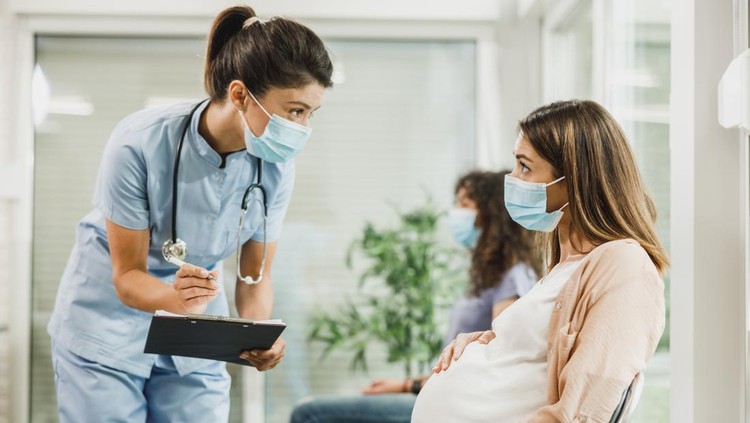 ilustrasi konsultasi Nurse talking to young pregnant woman and taking notes before covid-19 vaccine at hospital waiting room.