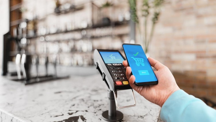 Man holding smartphone to the counter-top payment terminal for mobile payment in a cafe.