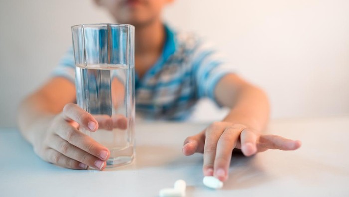 asian boy with cup of water and medicine in hand