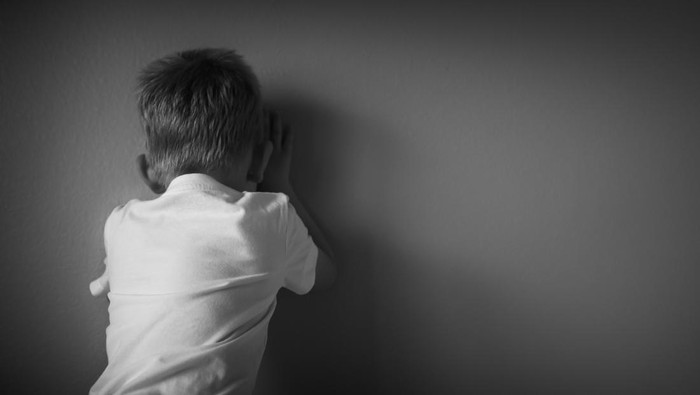 Sad little lonely boy facing a wall.