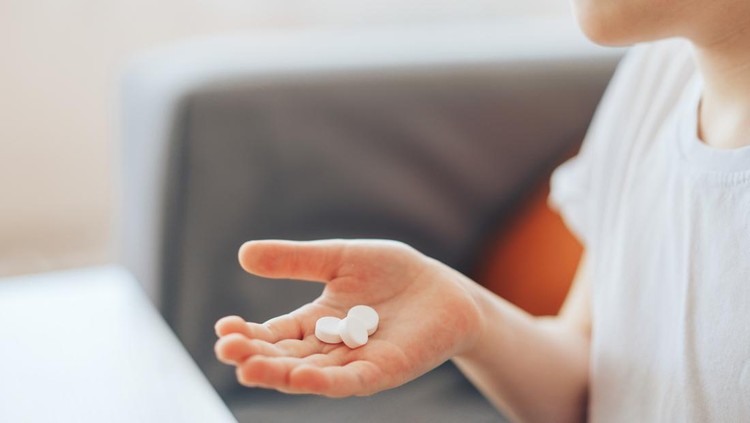 Boy holding white pills in his palm.