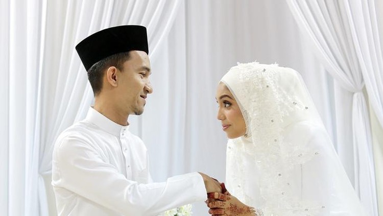 A Muslim young woman holding a young man's hand for 'salam' (gesture of mannerism in greeting) when they are certified newlywed in Islam 'akad nikah' (solemnisation) ceremony. In this ceremony, newlywed and all guests are required to wear pure white tradiitonal clothing.