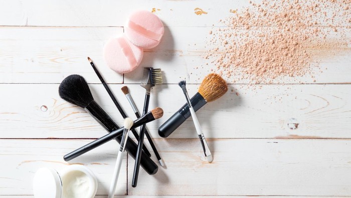 Concept of cosmetics and makeup with free powder, skincare and various professional make up face brushes over white wooden background for elegant beauty background, flat lay view