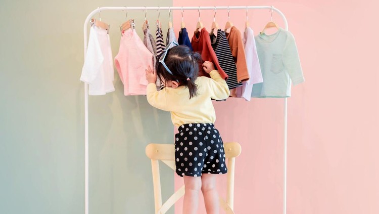 931577634 Soft Focus of a Two Years Old Child Choosing her own Dresses from Kids Cloth Rack