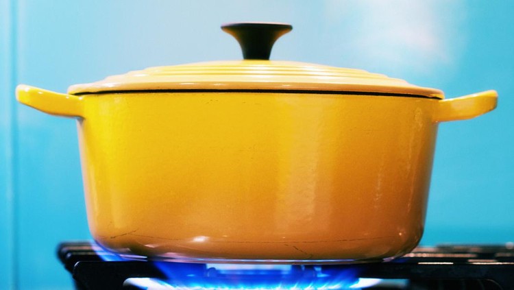 A yellow enamel casserole, with its lid on, sits on a lit gas burner creating steam as it heats.