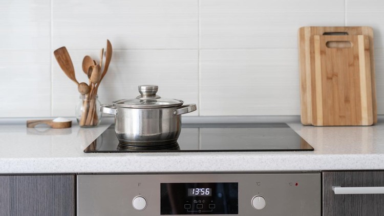 Black ceramic induction stove with timer on control panel and saucepan on top. Contemporary home with modern interior, built in kitchen appliance and white tile on wall with copy space