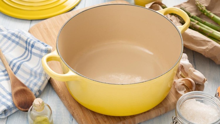 Yellow dutch oven on a wooden board with condiments around it