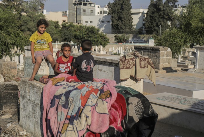 GAZA, PALESTINE - 2022/10/19: Palestinian children from the Kahil family play in front of their home in the Sheikh Shaaban cemetery in Gaza City. There is a battle for space between the living and the dead as the homeless settle in cemeteries. Camelia Kahil, a resident, said that if the dead could speak, they would tell them to get out of there. Due to poverty, they don't have a choice but to live in the cemetery and endure the pungent smell, which they call 