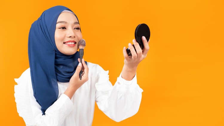 Beauty muslim woman with hijab applying makeup brush. Girl gets blush on the cheekbones.
