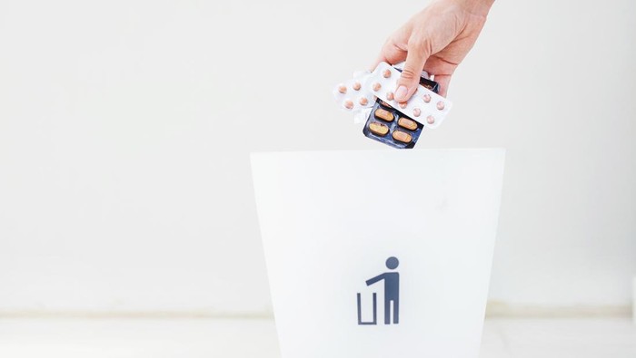 woman hand holding several package of pills over white bin for rubbish