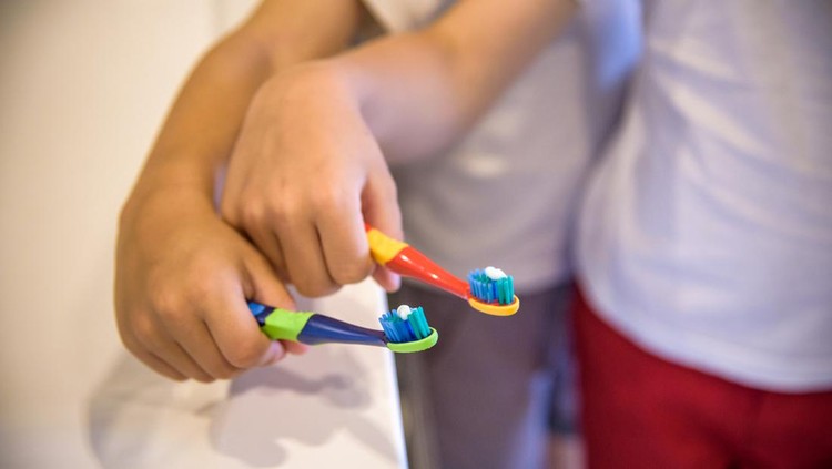 Child's hands holding toothbrush on pink backgroubd. Healty care teeth concept. Copy space for your text.