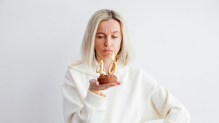 Adult unhappy beautiful woman forty years with festive cupcake with candle in hands in living room at the home party, birthday girl