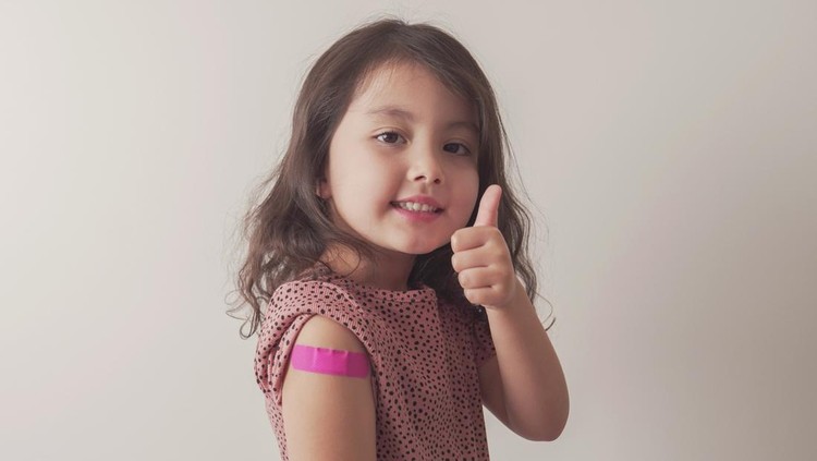Young mixed Asian girl giving thumb up and showing her arm with pink bandage after got vaccinated or inoculation, child under 12 years old immunization, health concept