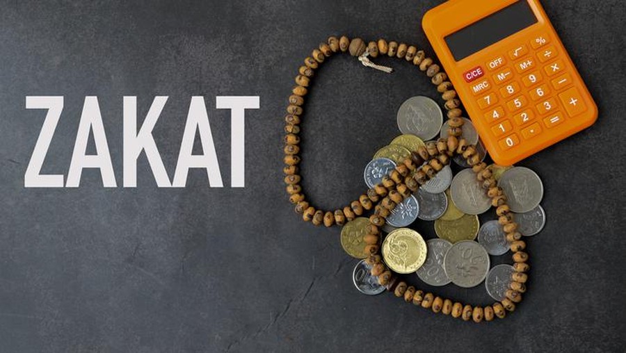 Top view of calculator, prayer beads and coins over black background written with ZAKAT