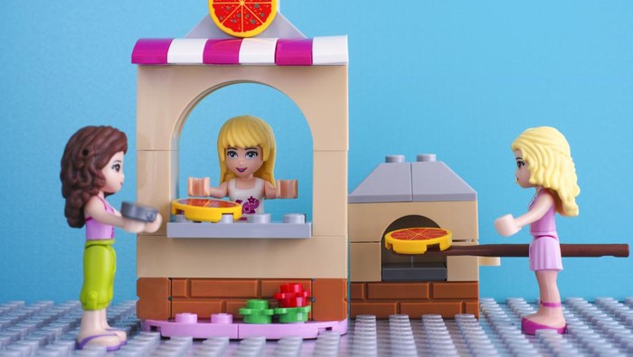 Tambov, Russian Federation - April 01, 2016: Lego Friends pizzeria. Brunette girl with coin buying pizza in pizzeria. Blonde girl baking pizza in oven. Studio shot. Blue background.