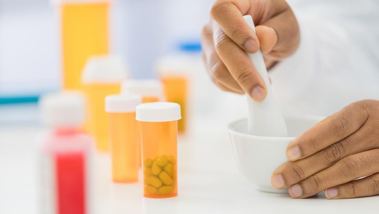 An unrecognizable female pharmacist uses a mortal and pestle to mix a custom medication for a patient.