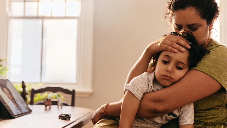 Compassionate mother caring for her sick son at home. Loving mother embracing her young son during an online consultation with their family doctor. Mother and son video calling their paediatrician.