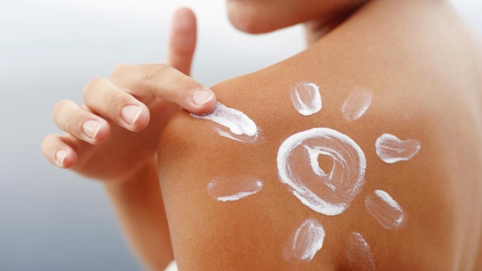 Dark tanned body of young woman in summer with sunscreen  lotion in shape of sun