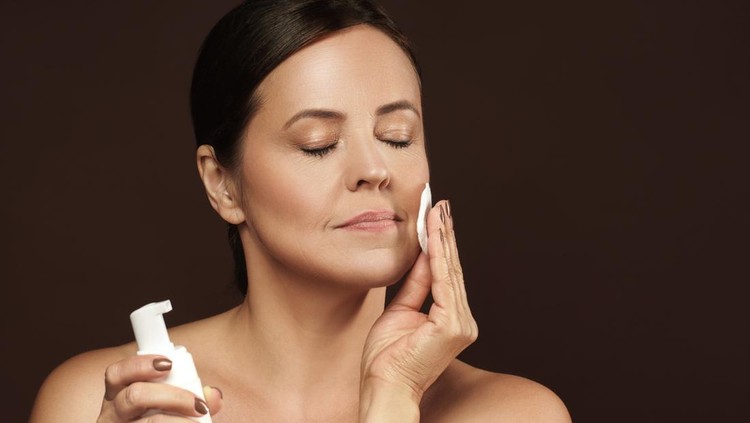 1310460541 Portrait of a beautiful middle aged woman with a cotton pad and bottle of cleansing liquid