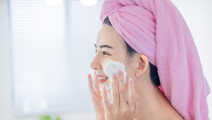 asian beauty woman with towel on head is cleaning her face by facial cleanser in the bathroom